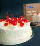 Decorative cake with cherries on top next to a box of Crust & Crumbs White Forest Cake Mix.