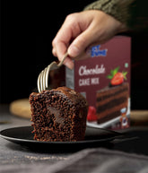 Chocolate cake being cut with a fork on a plate, with a box of Crust N Crumbs chocolate cake mix in the background.